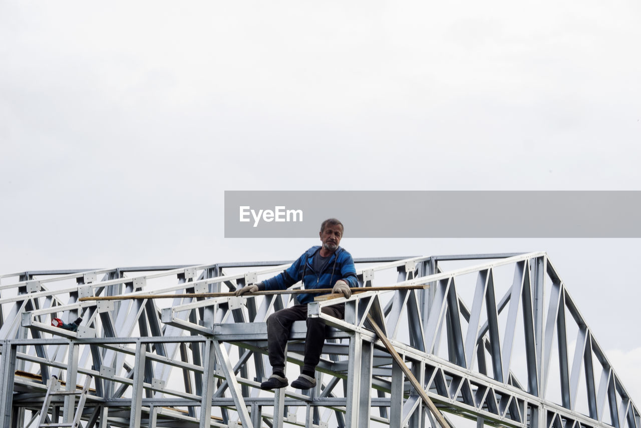 Low angle view of man sitting on bridge against sky