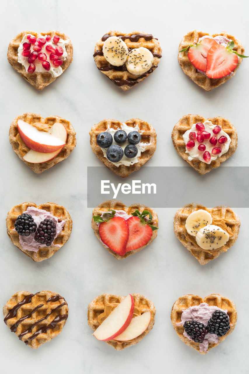 Several mini heart shaped waffles with various toppings.