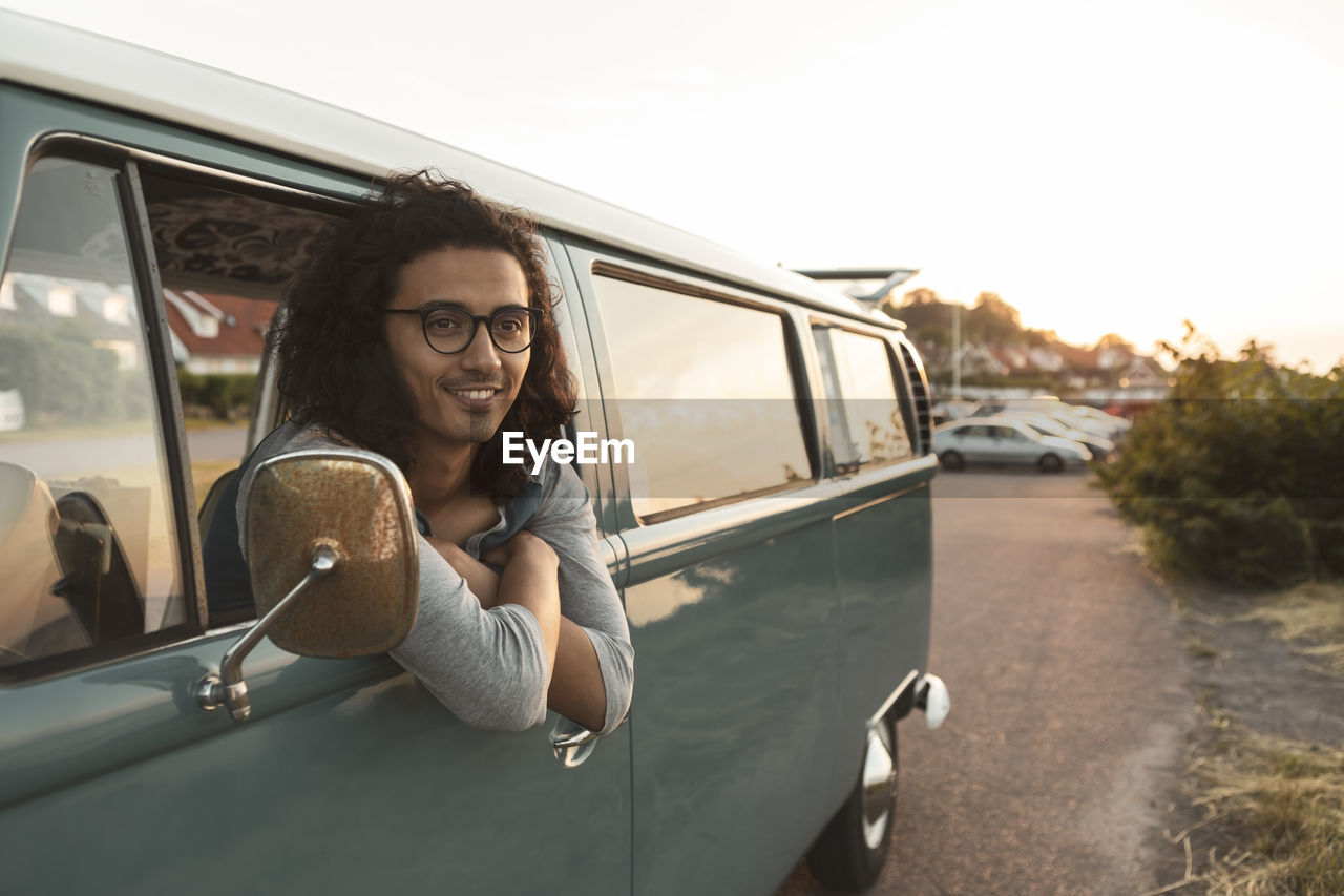 Smiling man looking away while sitting in camping van