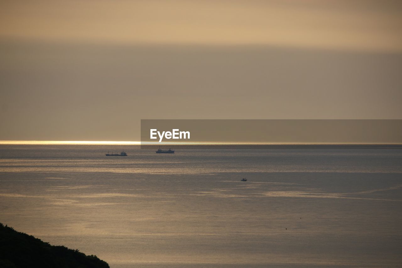 Distant ships in sea at sunset