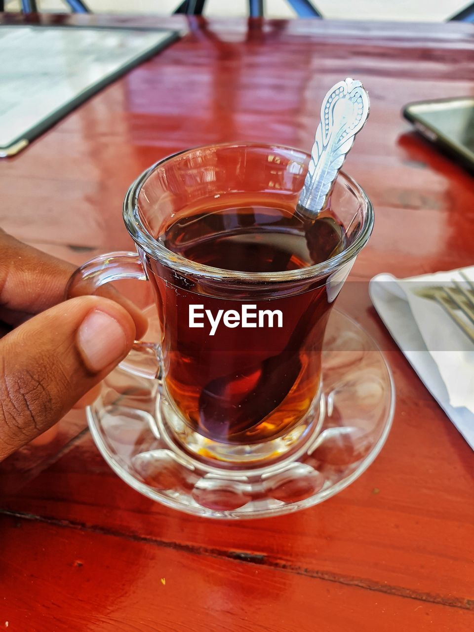 CROPPED IMAGE OF PERSON HOLDING GLASS OF TEA ON TABLE