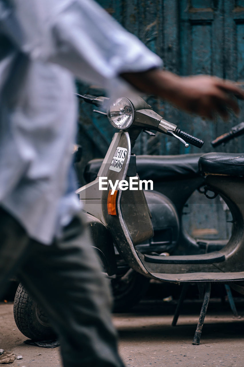 Midsection of man walking against motor scooter on road