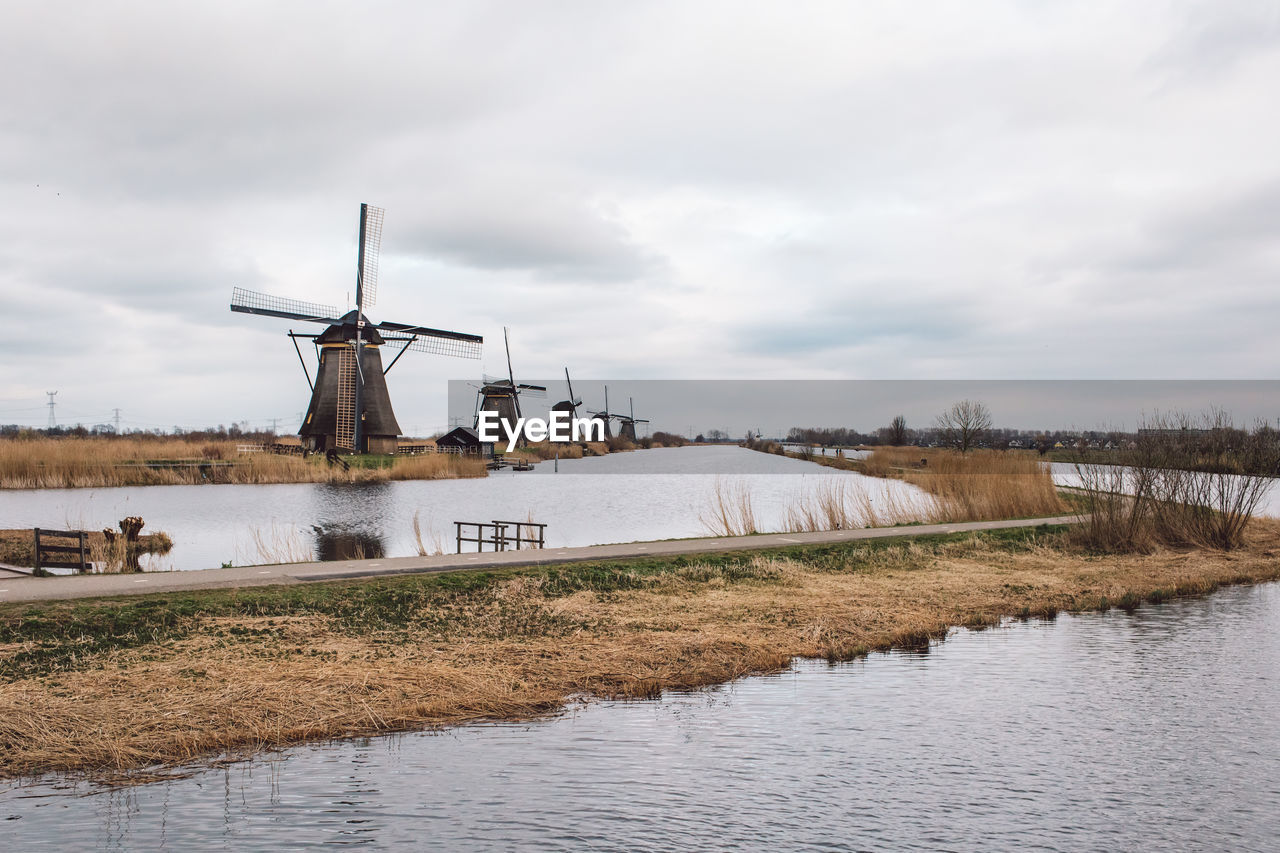 Traditional windmill by canal against sky