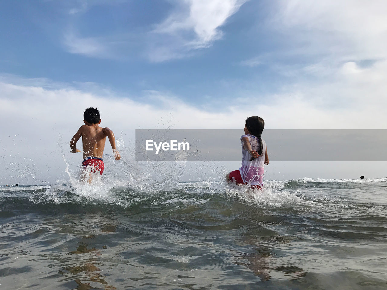 Rear view of men enjoying in sea against sky