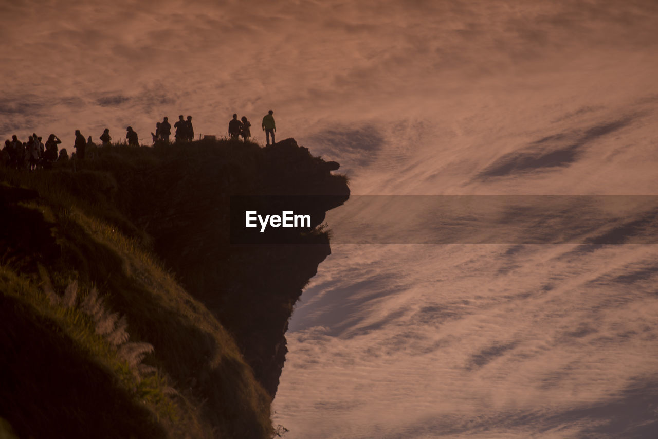 Low angle view of people at cliff against cloudy sky