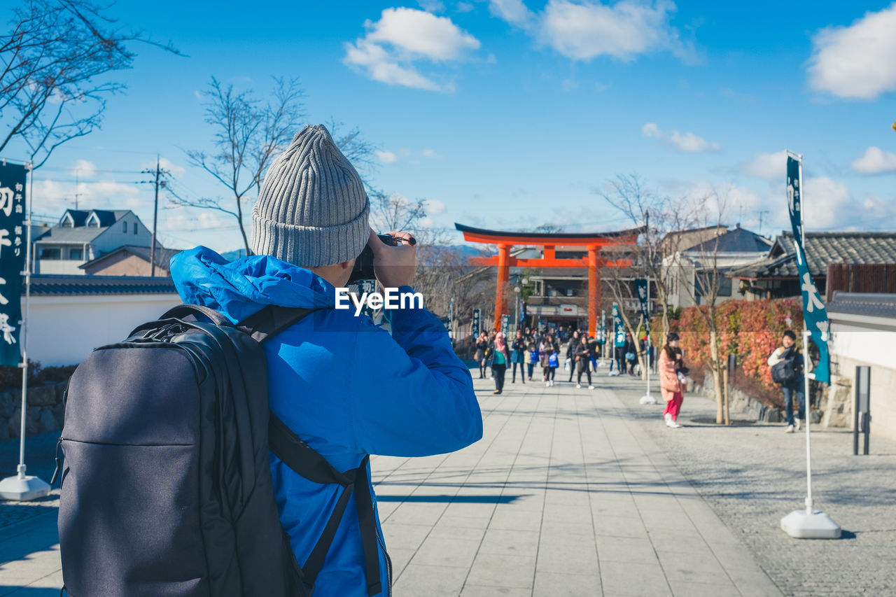 Rear view of photographer photographing people and torii gate while standing on footpath