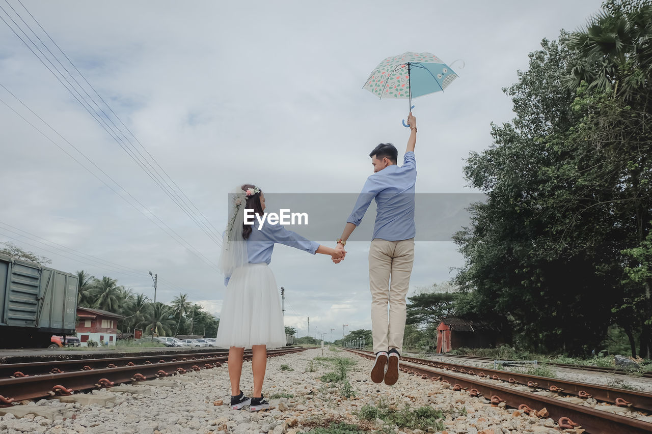 PEOPLE STANDING BY RAILROAD TRACK AGAINST SKY