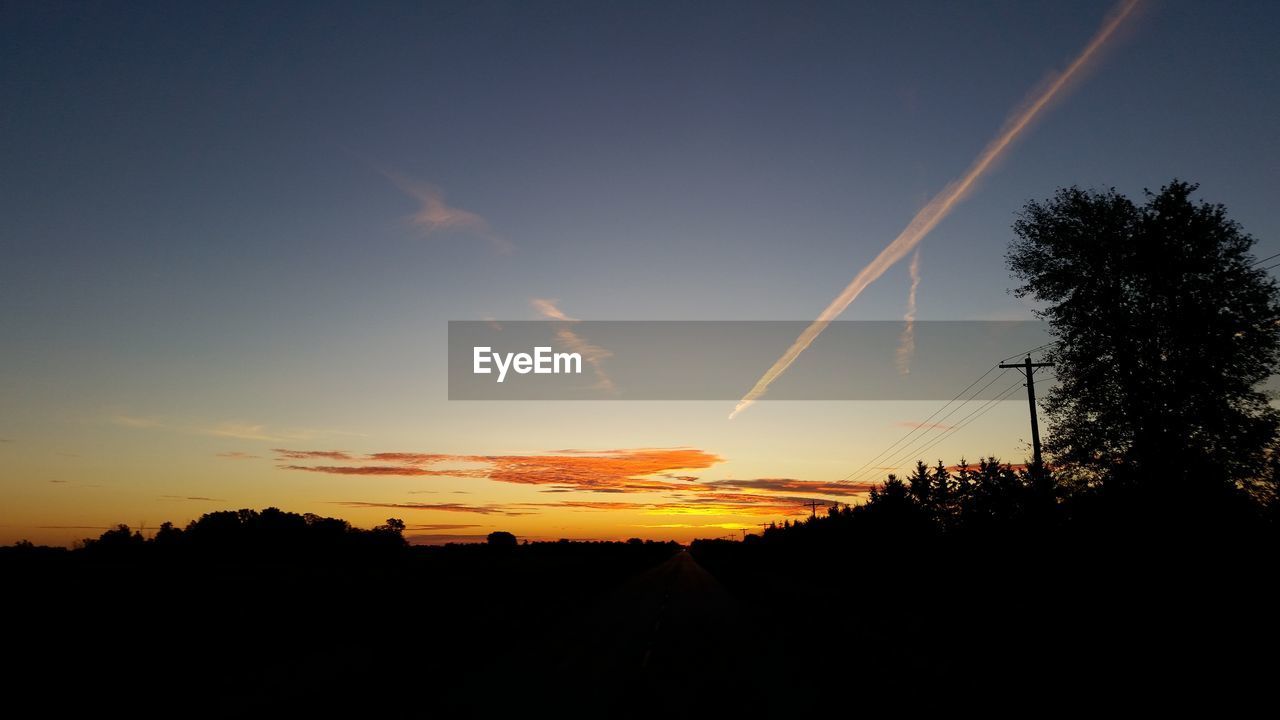 SILHOUETTE LANDSCAPE AGAINST VAPOR TRAILS IN SKY