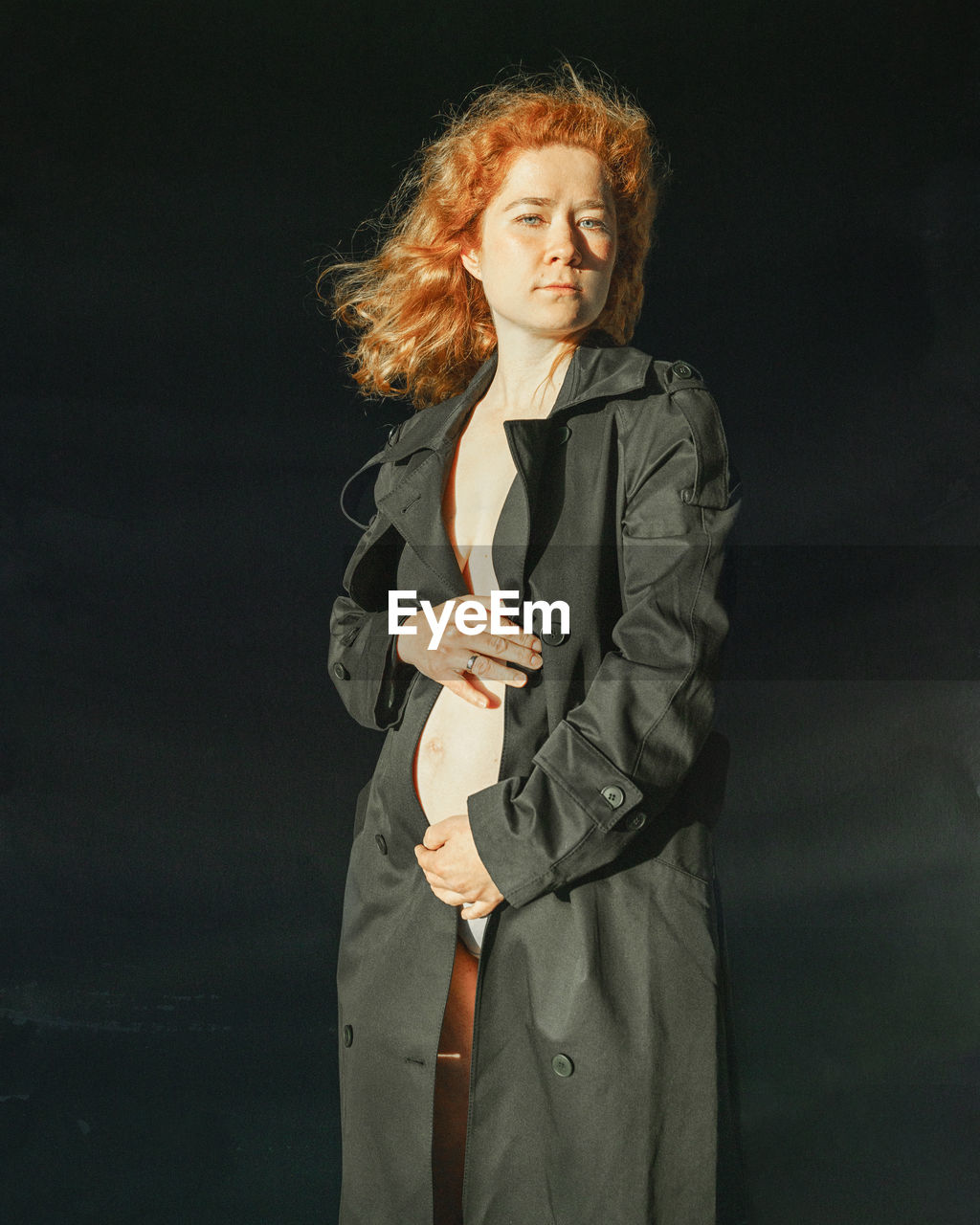 Portrait of young pregnant woman standing against black background 