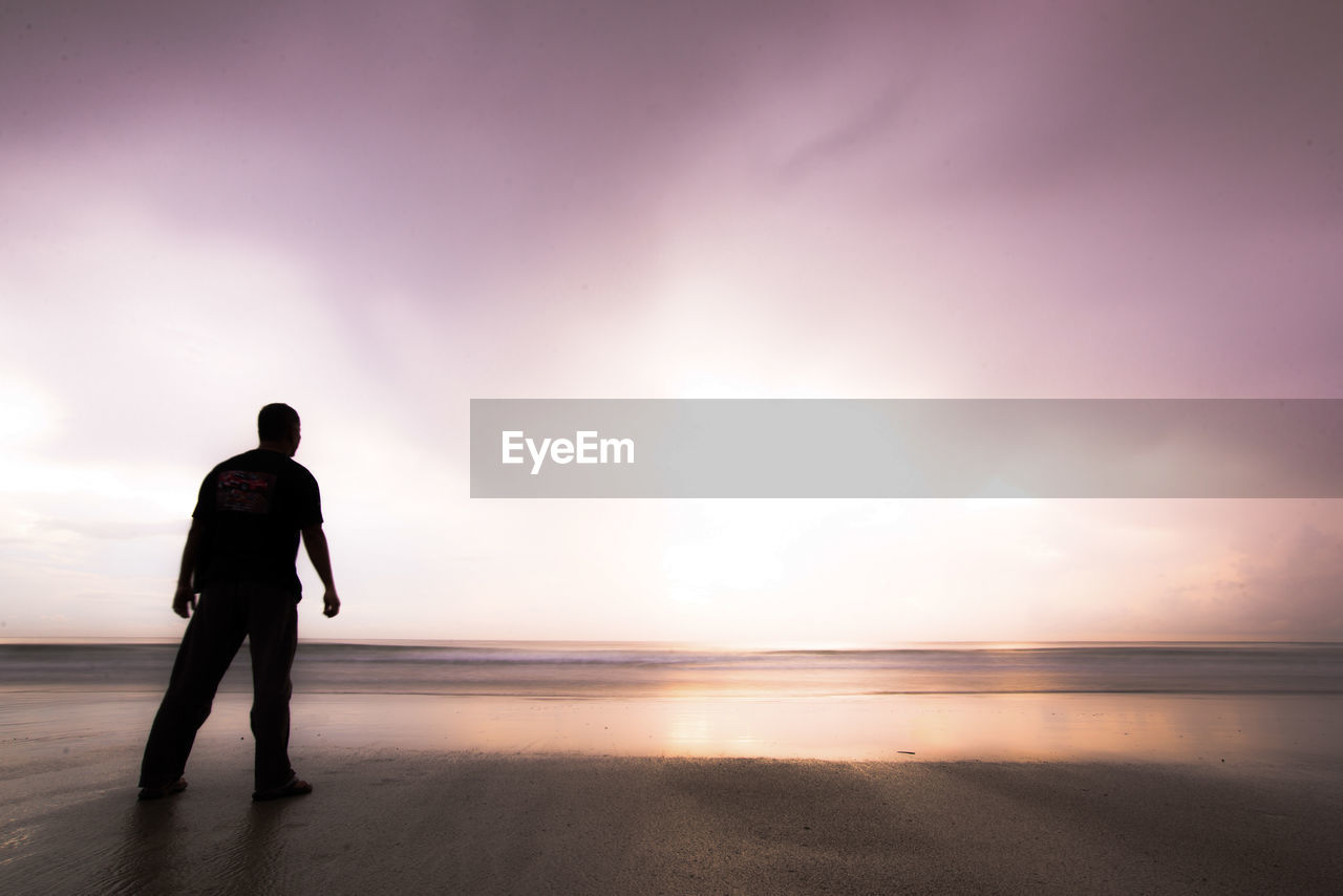 Silhouette man standing on beach against sky during sunset