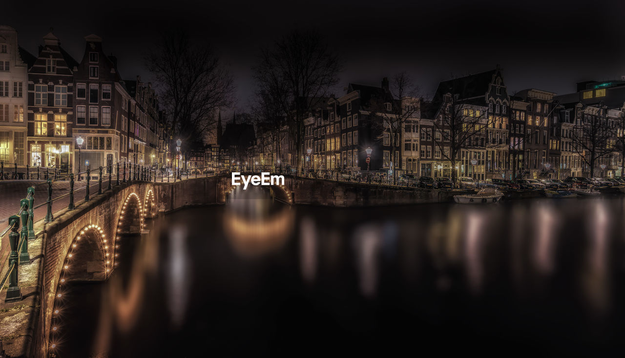 Arch bridge over river by illuminated buildings against sky at night