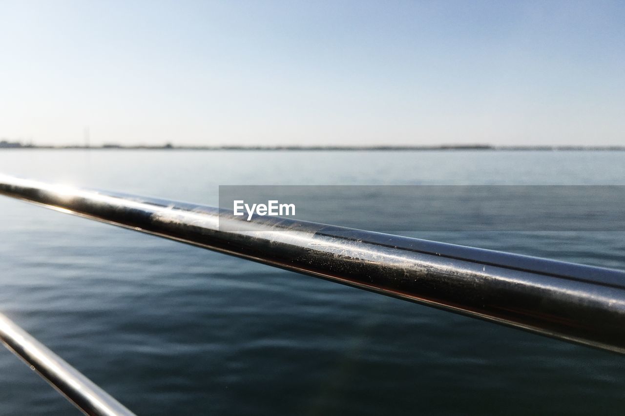 Close-up of railing by river against clear sky