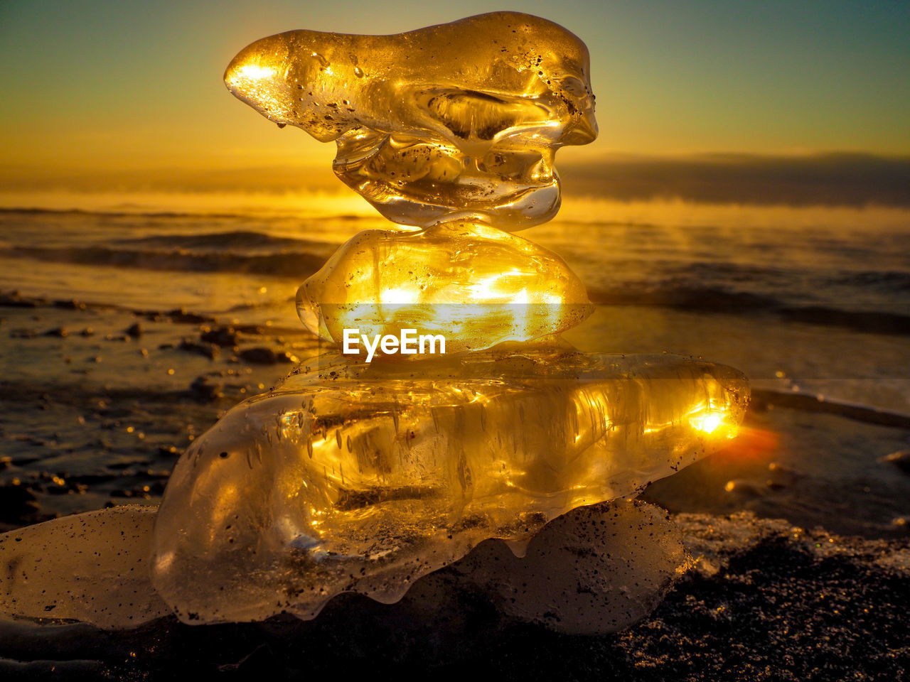 ILLUMINATED STATUE ON BEACH AGAINST SKY DURING SUNSET