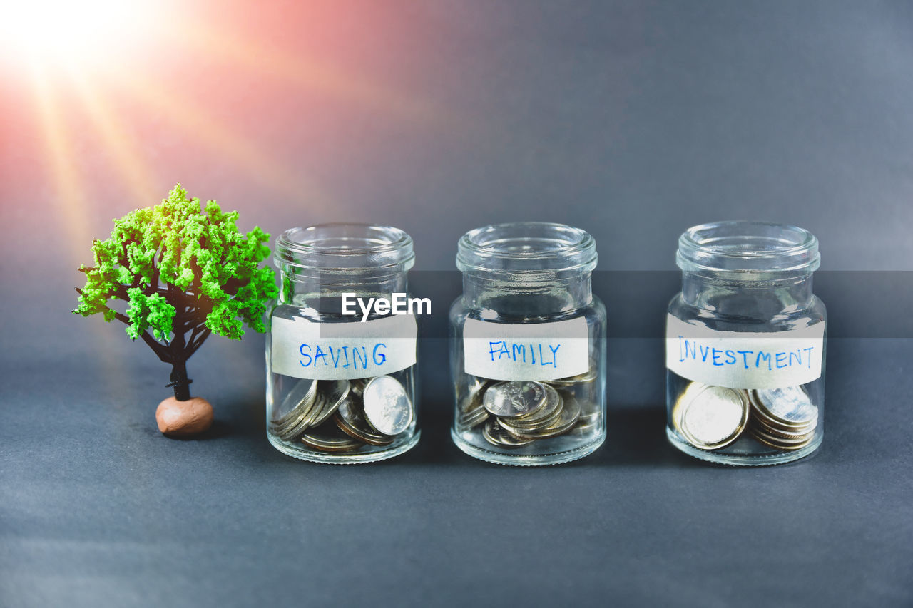 CLOSE-UP OF COINS IN JAR ON TABLE AGAINST WALL