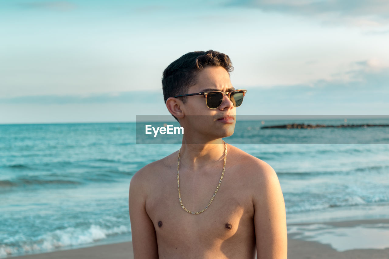 YOUNG MAN WEARING SUNGLASSES STANDING AT BEACH