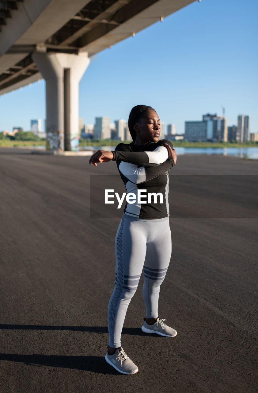 African american sportswoman warming up under bridge