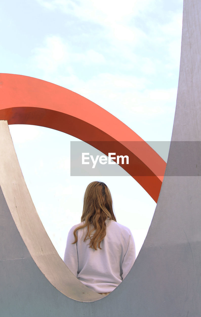 Rear view of woman seen through built structure standing against sky