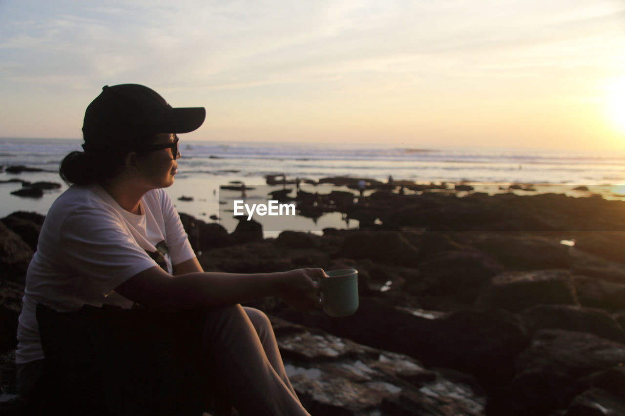 A women sitting on the beach against sky during sunset