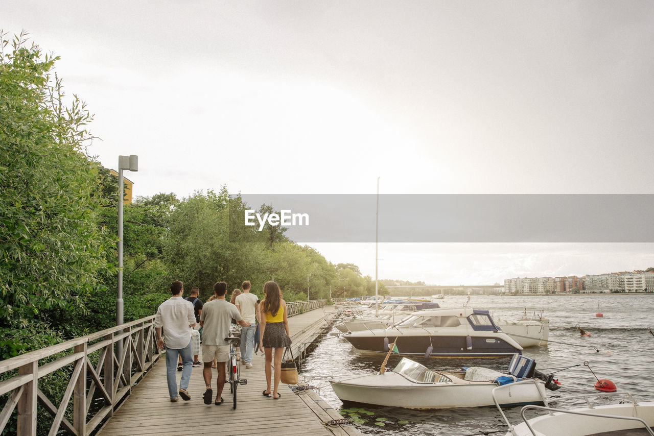 Rear view of male and female friends walking together on pier near marina