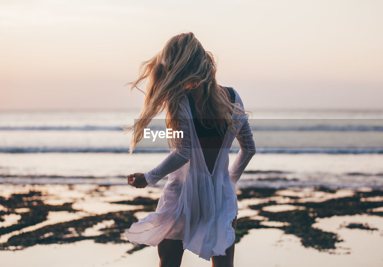 Rear view of woman at beach against clear sky during sunset