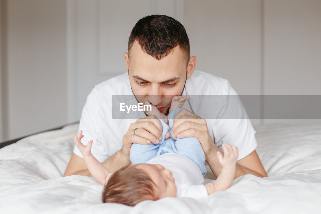 Father playing with baby daughter lying on bed at home