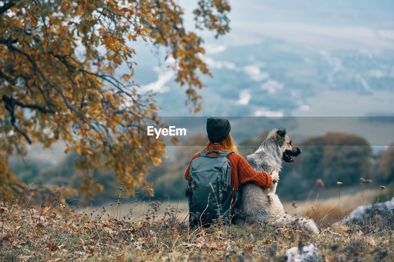 REAR VIEW OF MAN SITTING ON ROCK DURING AUTUMN