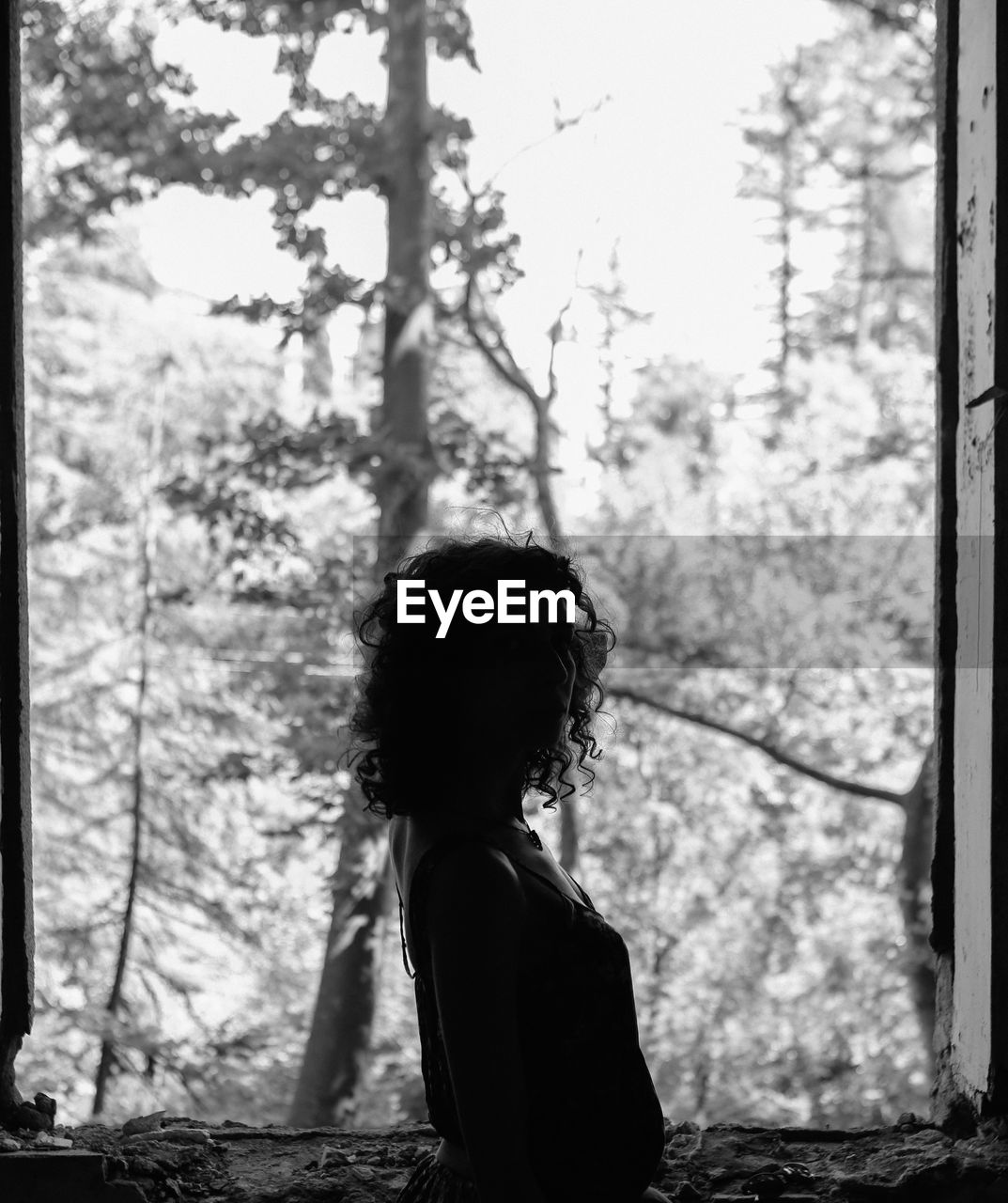 Side view of woman standing at abandoned window against trees
