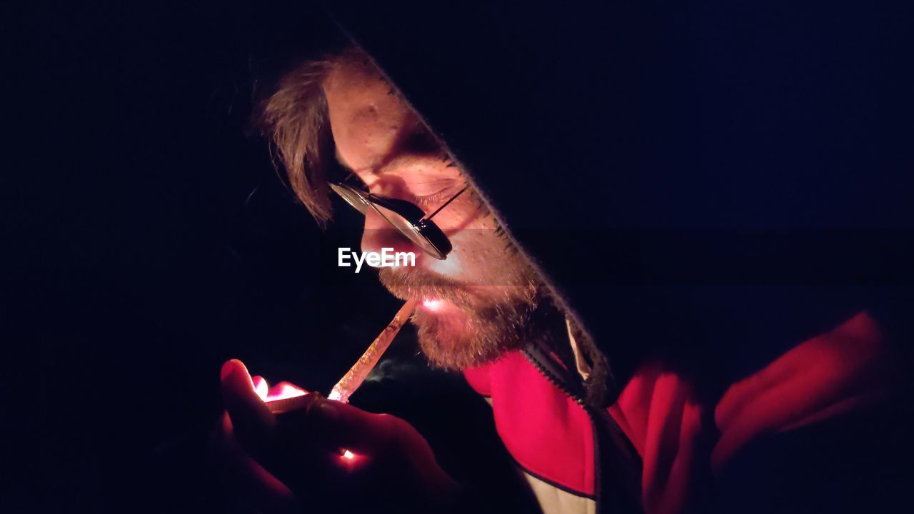 Midsection of man smoking cigarette against black background