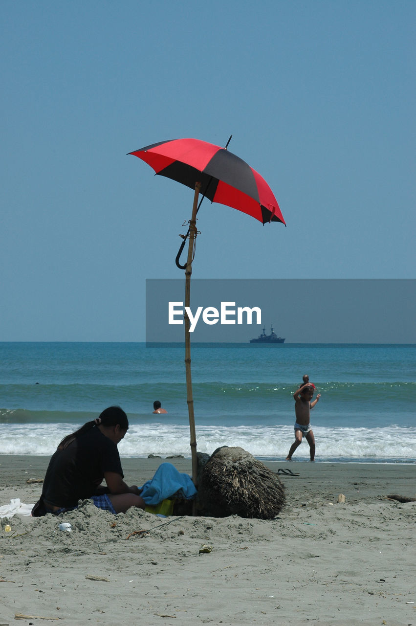 Woman sitting under umbrella tied to stick at beach