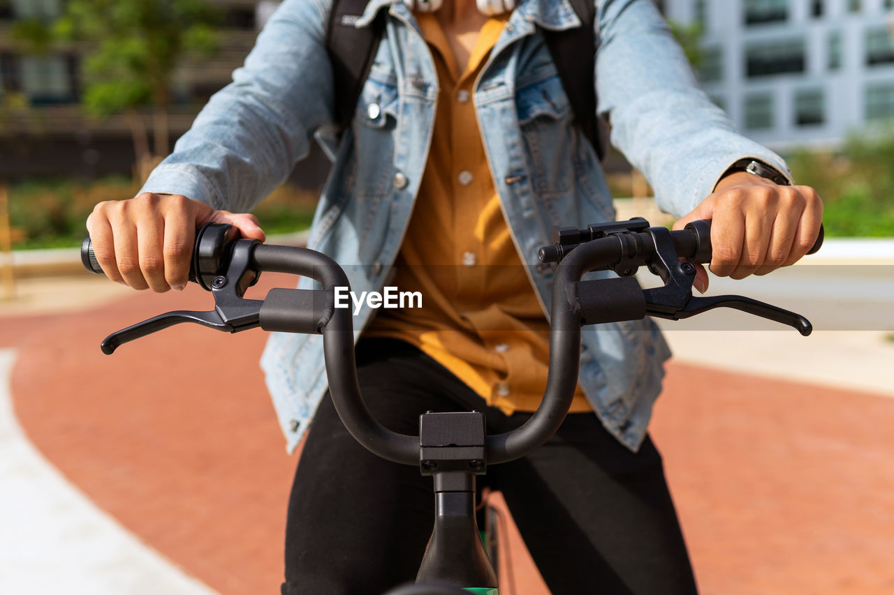 Crop unrecognizable ethnic male riding contemporary bike along street in city