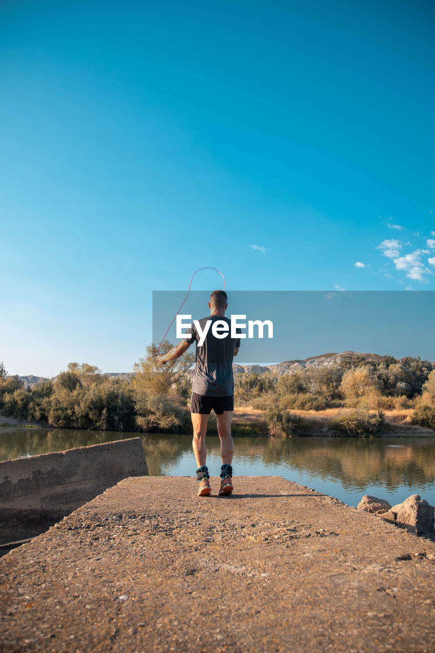 REAR VIEW OF MAN STANDING AGAINST SKY