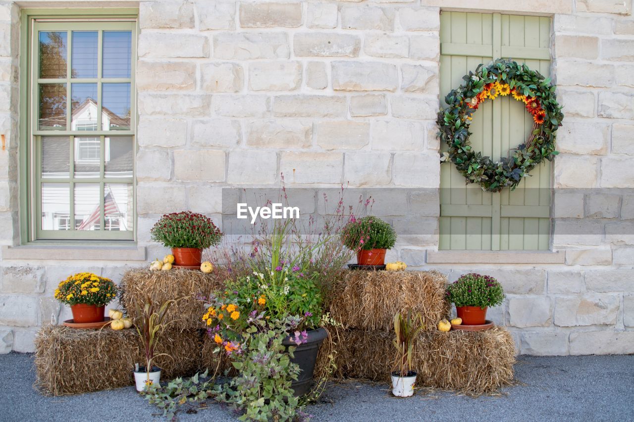 Fall harvest porch decor with colorful mums stacked on hay bales. an autumn wreath hung on a window.
