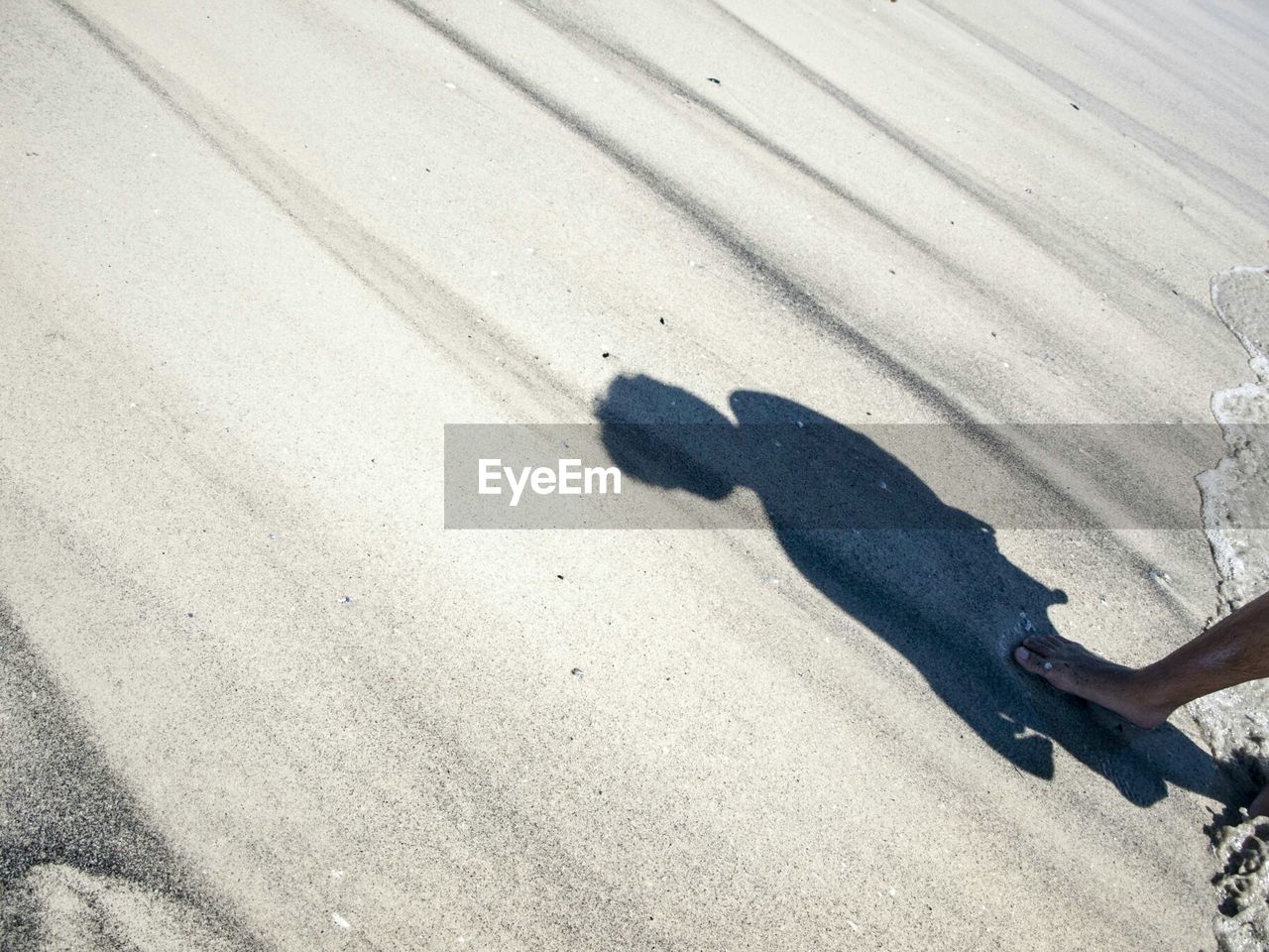 Low section of person at sandy beach with shadow