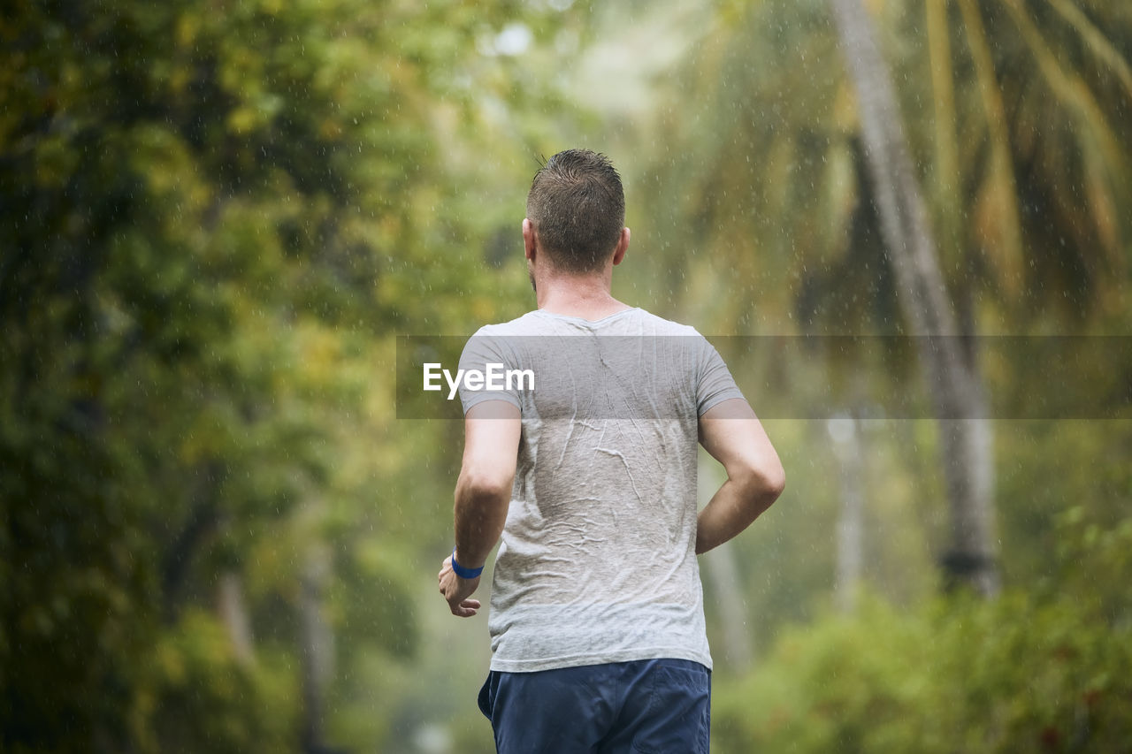 Rear view of runner in heavy rain. drenched young man runing in nature.