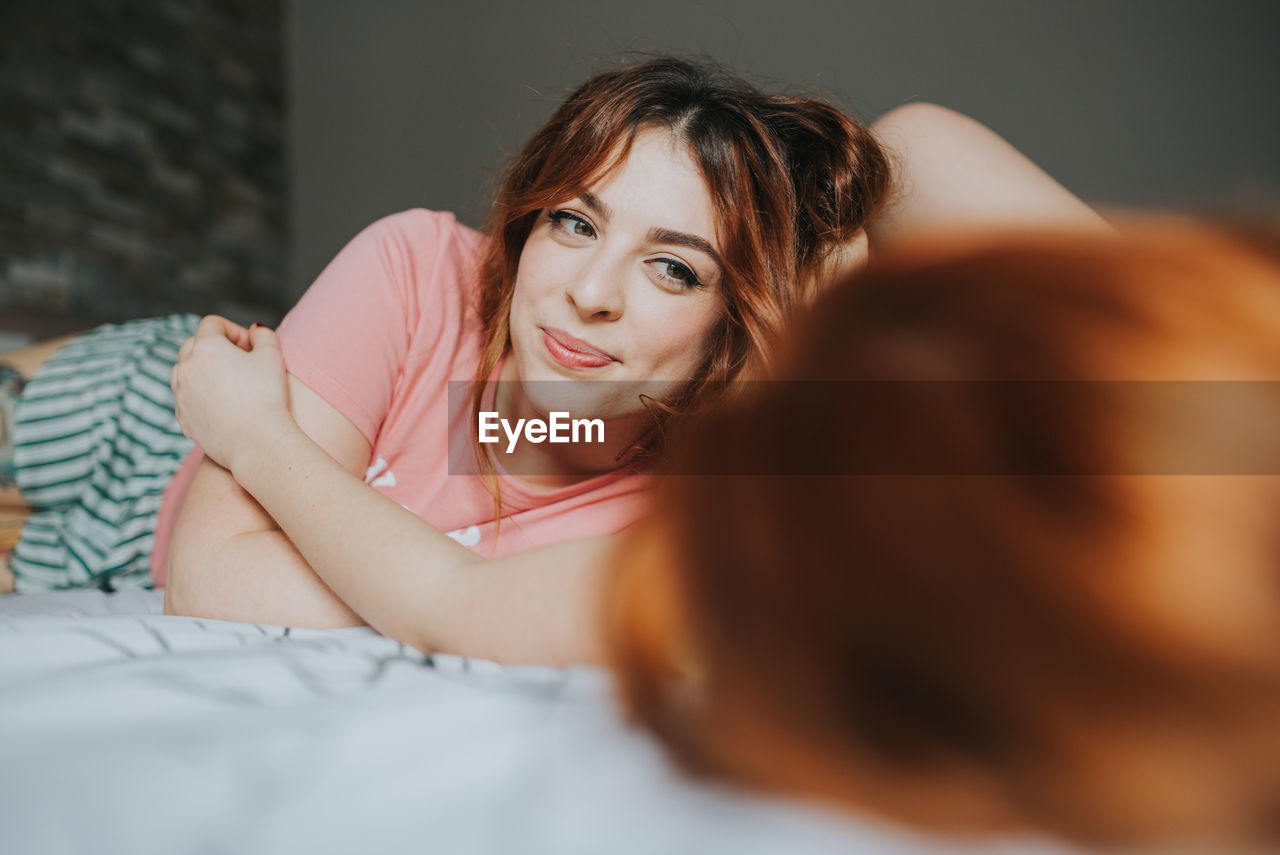 Crop young female girlfriends in pajamas relaxing on bed in bedroom