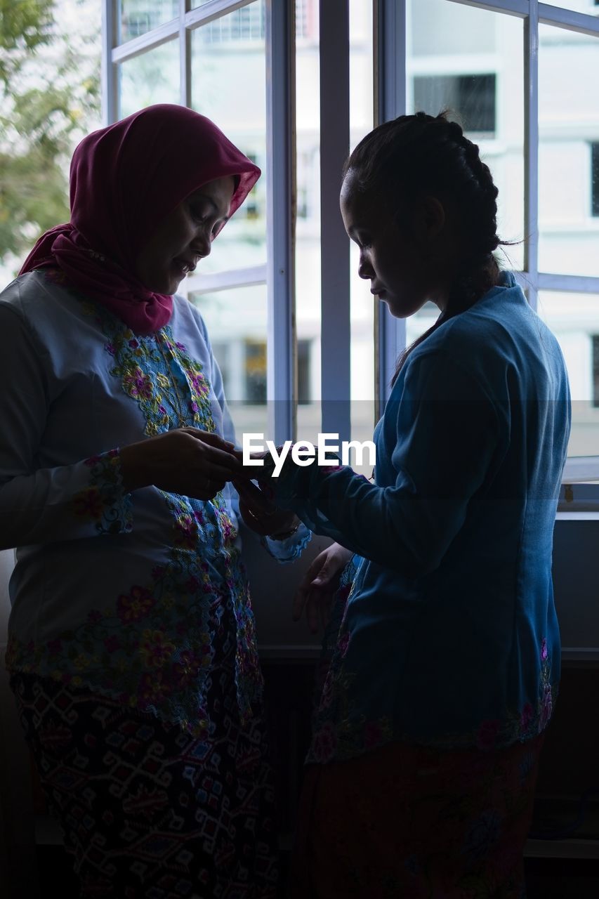 Woman wearing traditional clothing standing with daughter at home