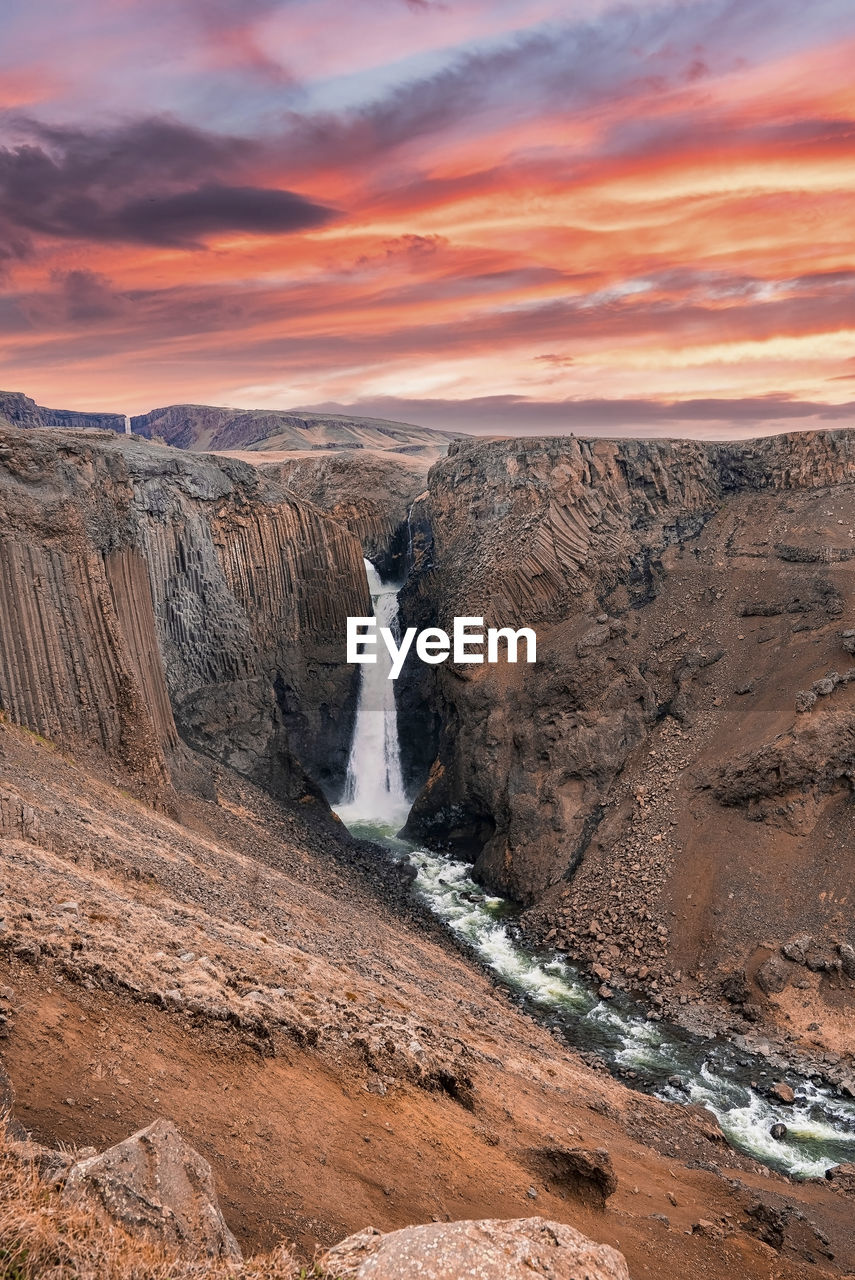 Cascades of litlanesfoss waterfall amidst basalt columns against sky at sunset