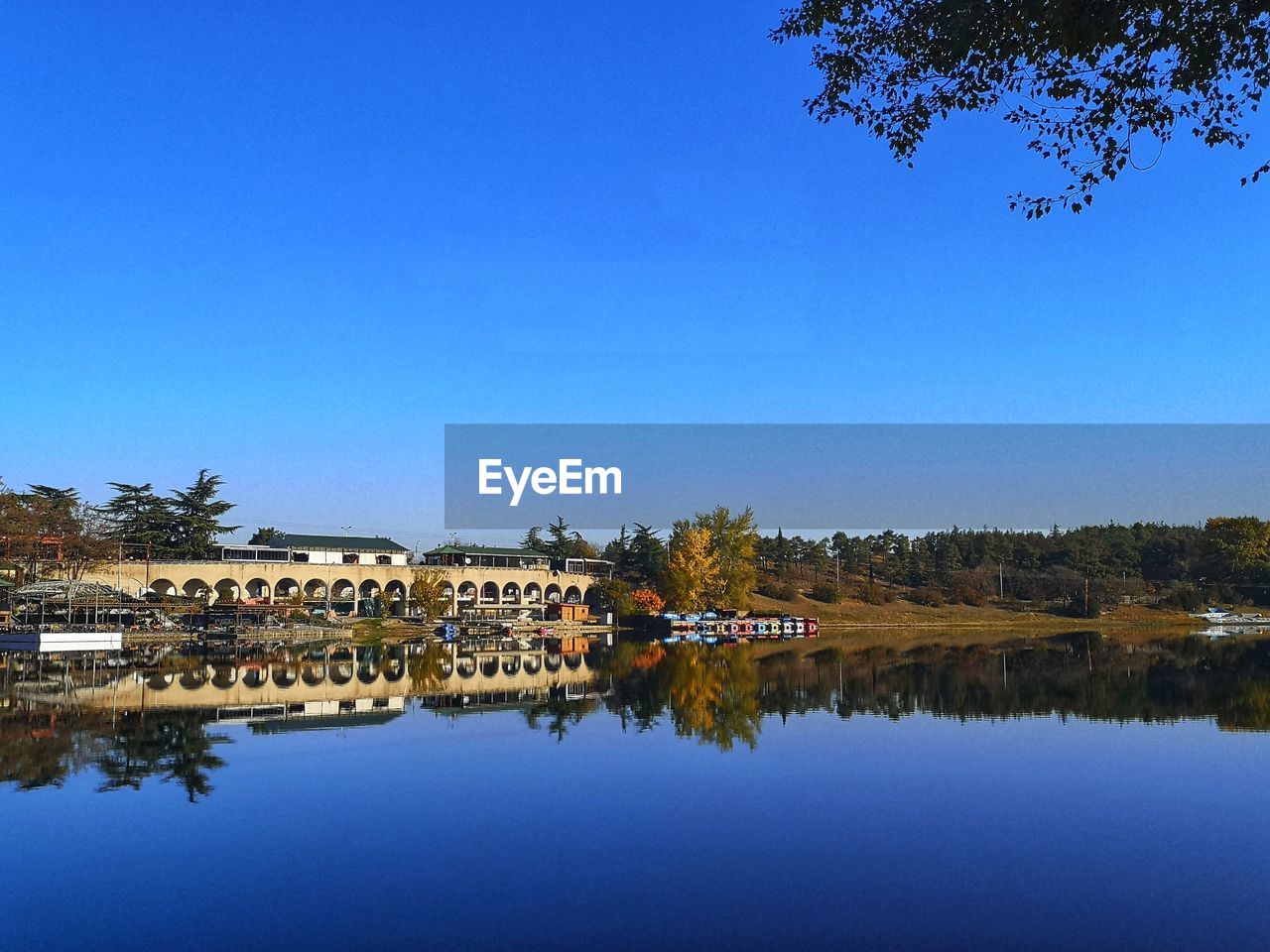 Reflection of building and trees in lake against clear blue sky