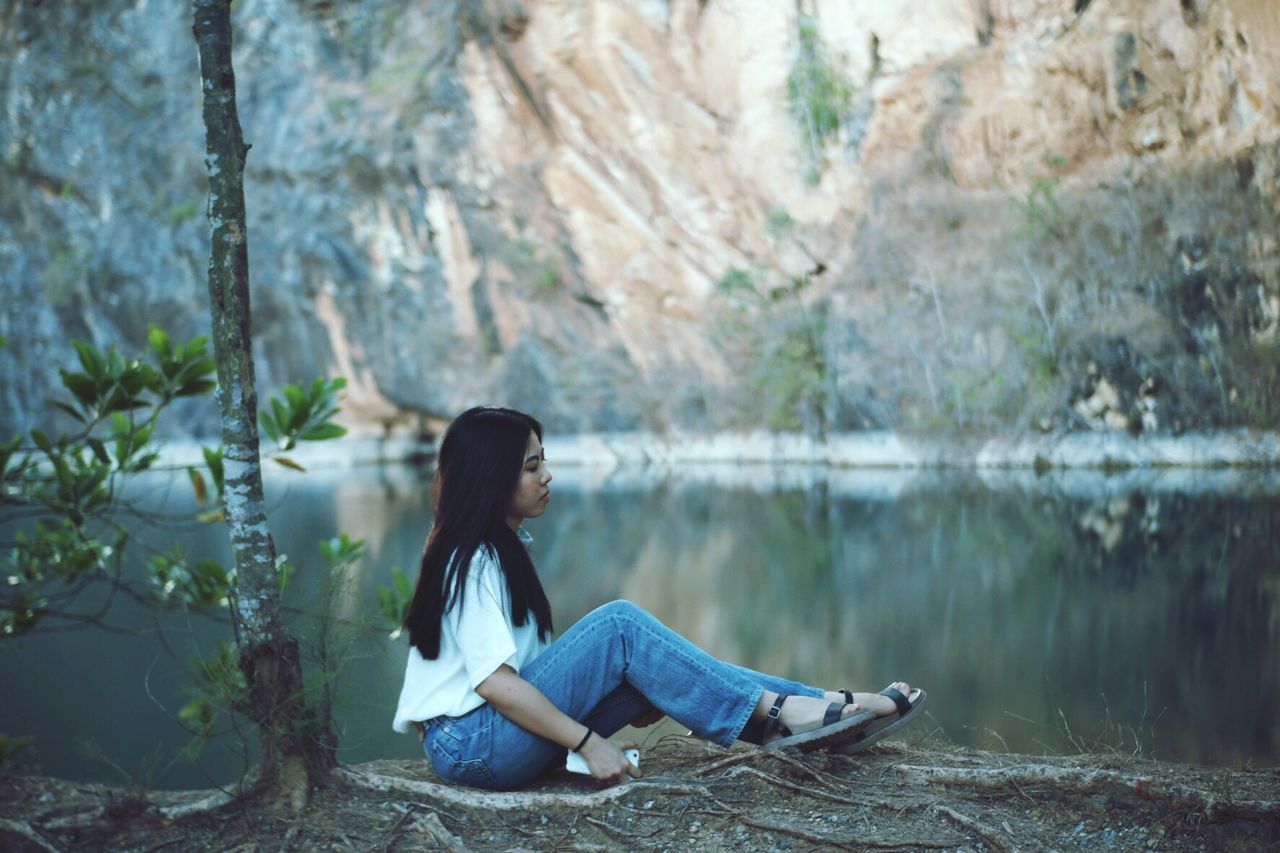 Side view of woman sitting by lake against rocks
