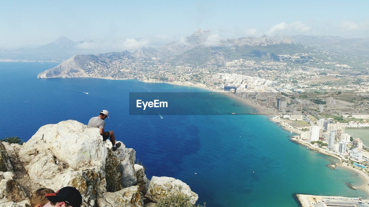 High angle view of man sitting on calpe rock by sea