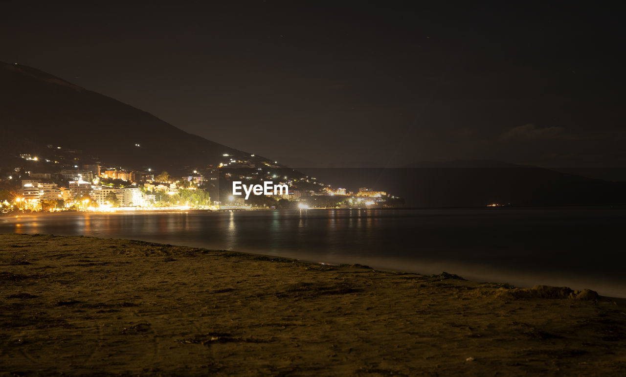 ILLUMINATED CITY BY SEA AT NIGHT