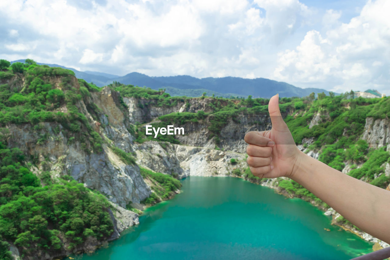 Cropped hand of woman gesturing thumbs up against landscape