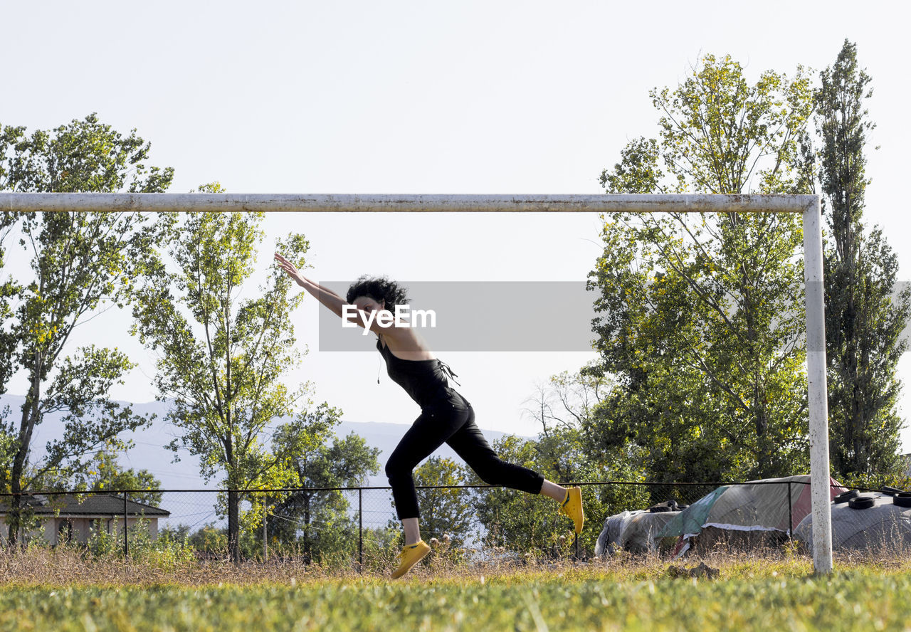 Side view of woman jumping on football field against sky