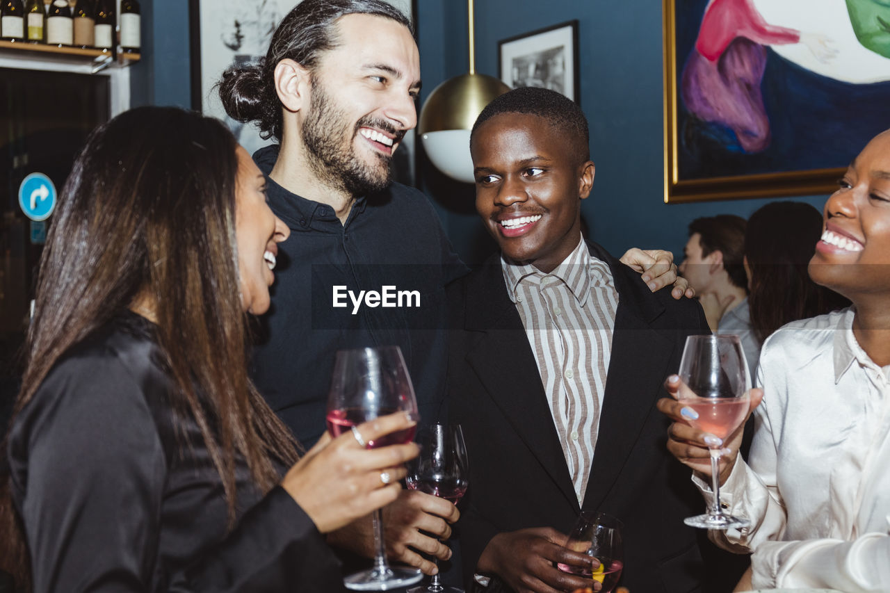 Happy male and female friends celebrating while having wine in restaurant