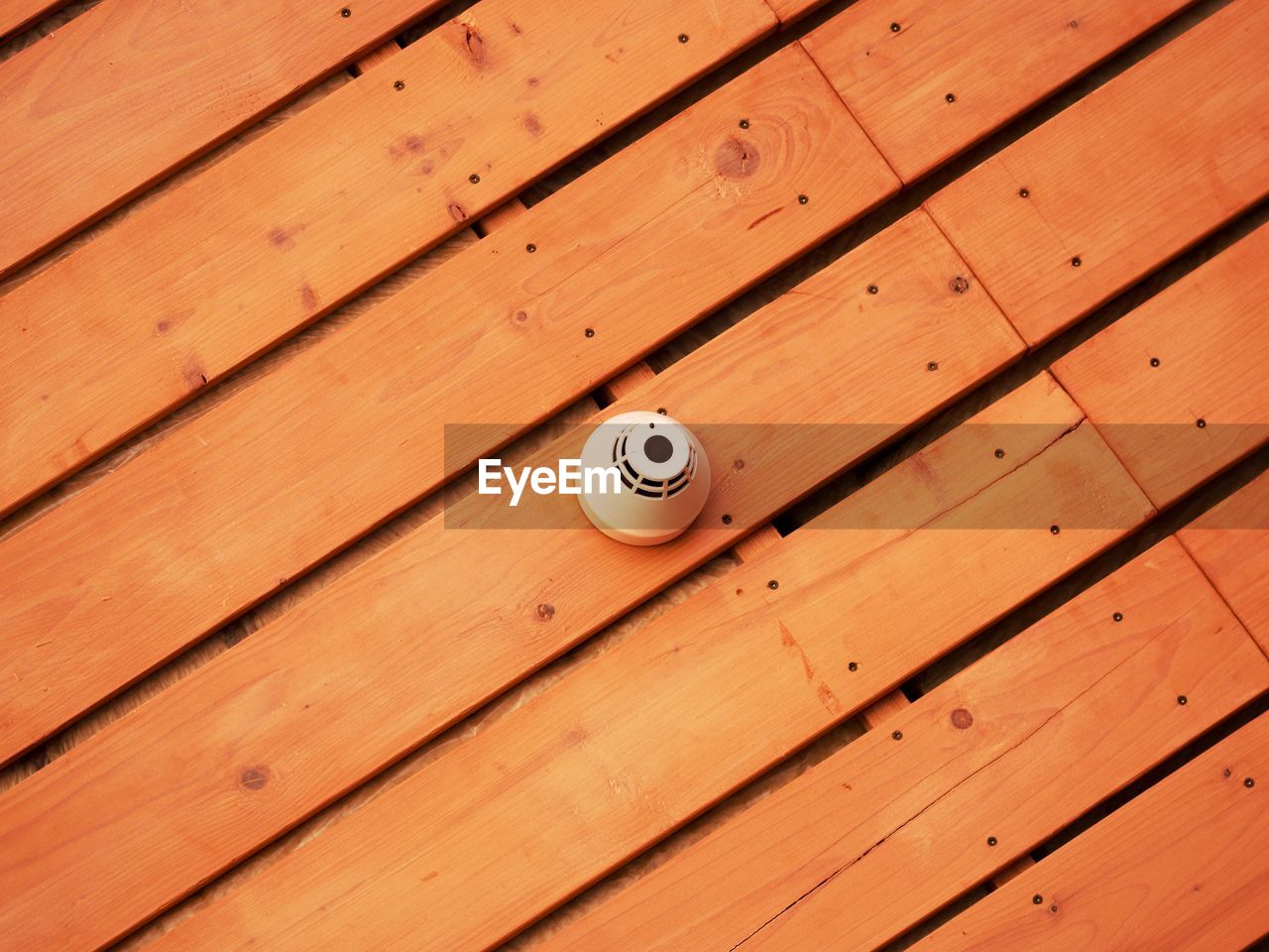 Smoke detector on ceiling wooden planks. gym hall ceiling with plastic smoke controler.