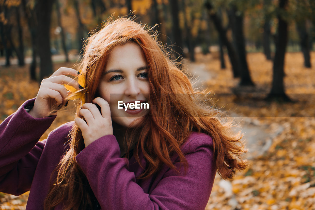 Autumn portrait of candid beautiful red-haired girl with fall leaves in hair.