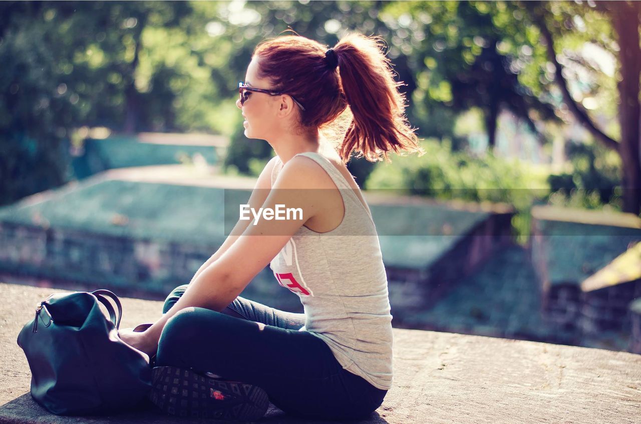 Woman with shoulder bag sitting on retaining wall