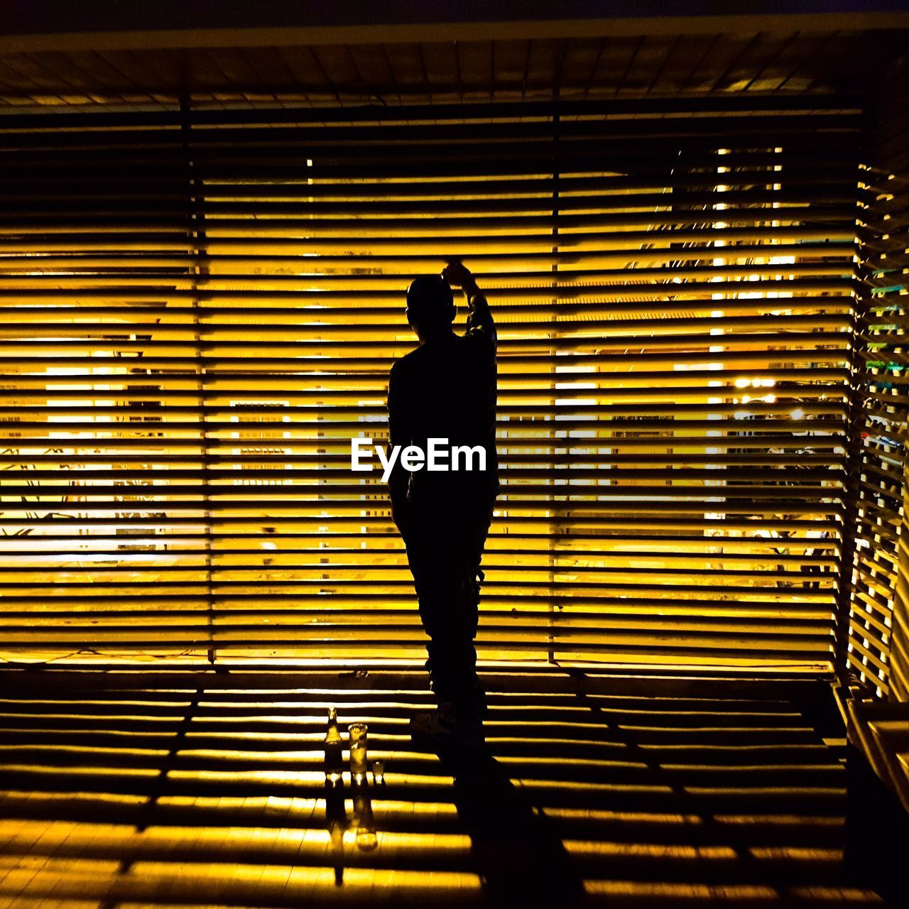 Rear view of silhouette man looking through window blinds