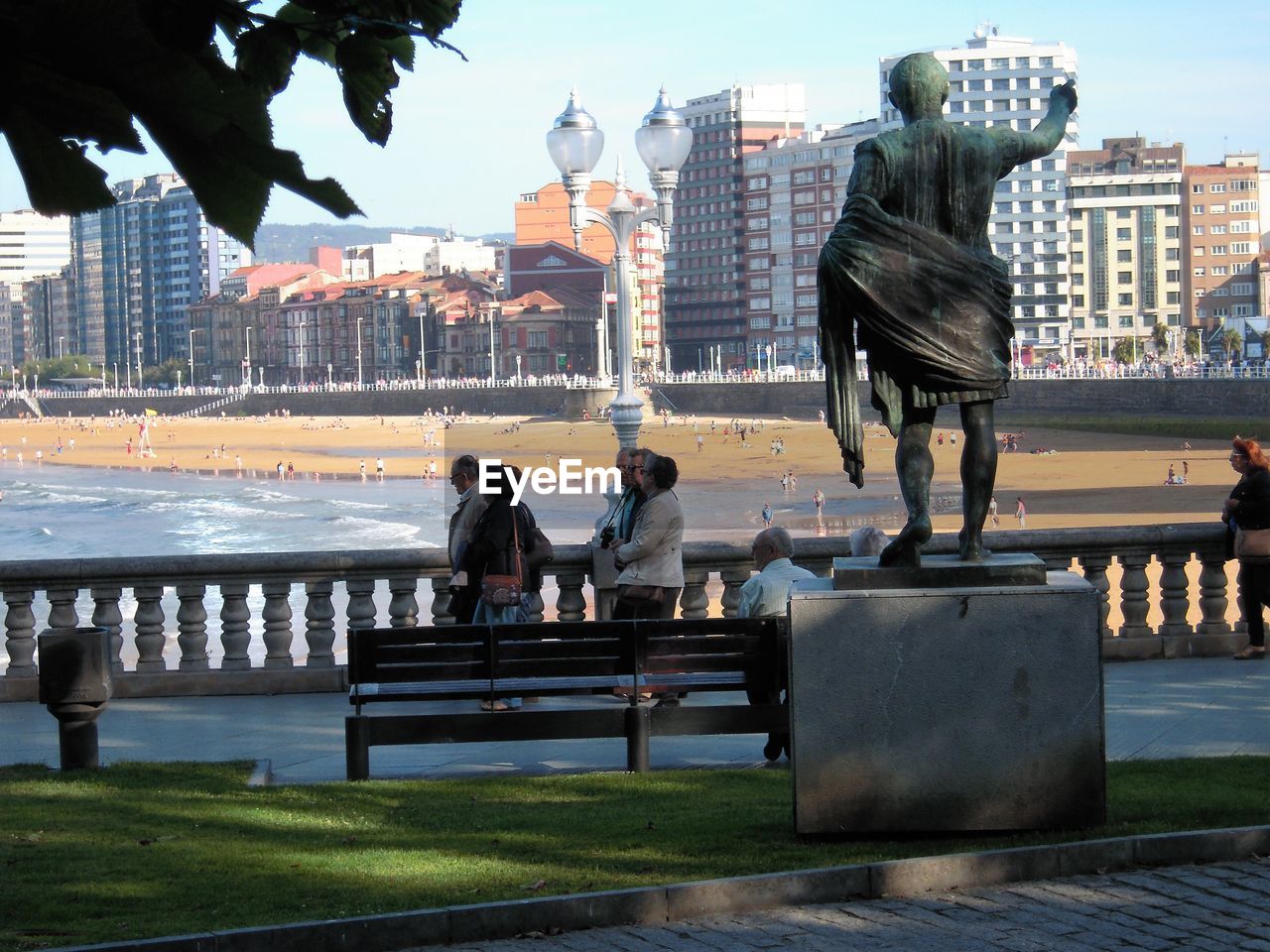 WOMAN SITTING BY SCULPTURE IN CITY AGAINST SKY IN BACKGROUND