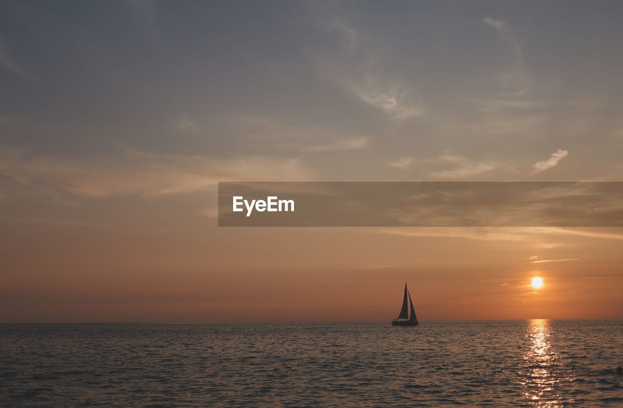 Sailboat in sea against sky during sunset